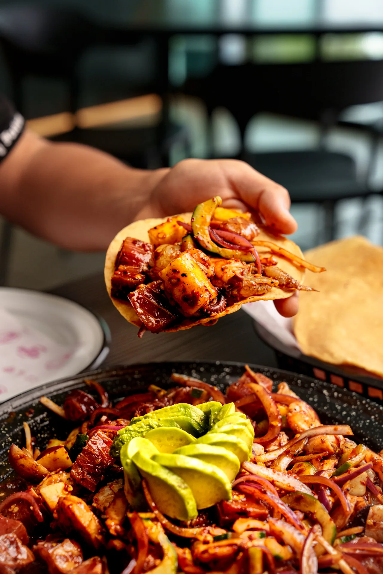 Mano levantando un bocado de carne sazonada sobre una charola con una rosa de aguacate
