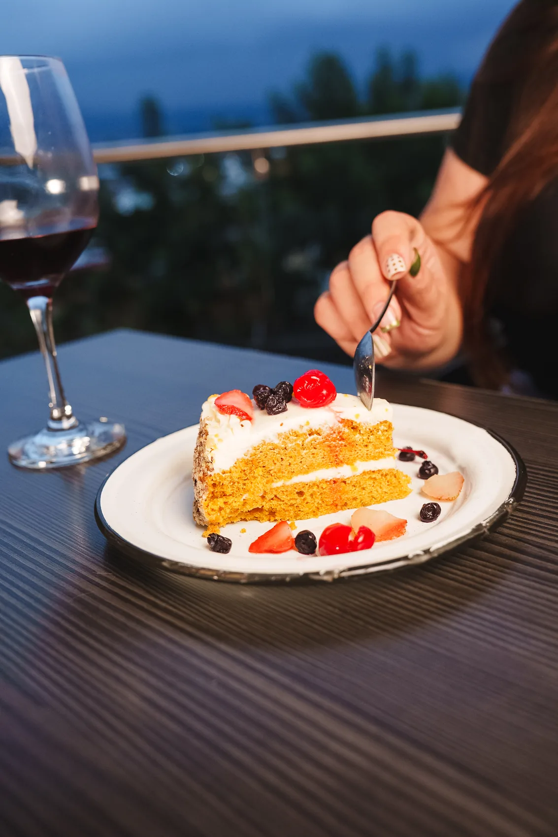Rebanada de pastel con fresas, una copa de vino tinto y un tenedor sobre la mesa de la terraza
